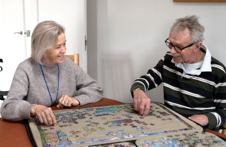 A volunteer sitting at a table doing a puzzle with the cared-for