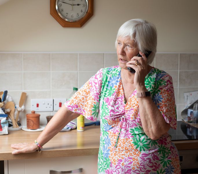 An older carer talking on the phone in her kitchen