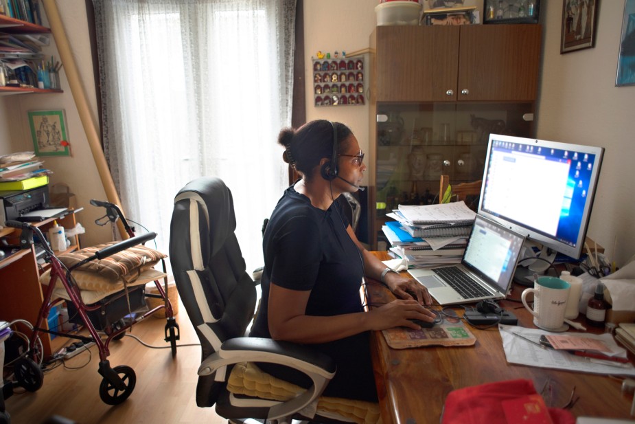 A black carer working from home surrounded by computers with a walker in the background