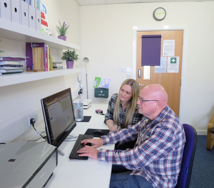 A carer sits next to a tutor taking a course in computing