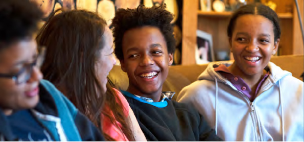 A young blac family sit together on the settee laughing and joking with each other